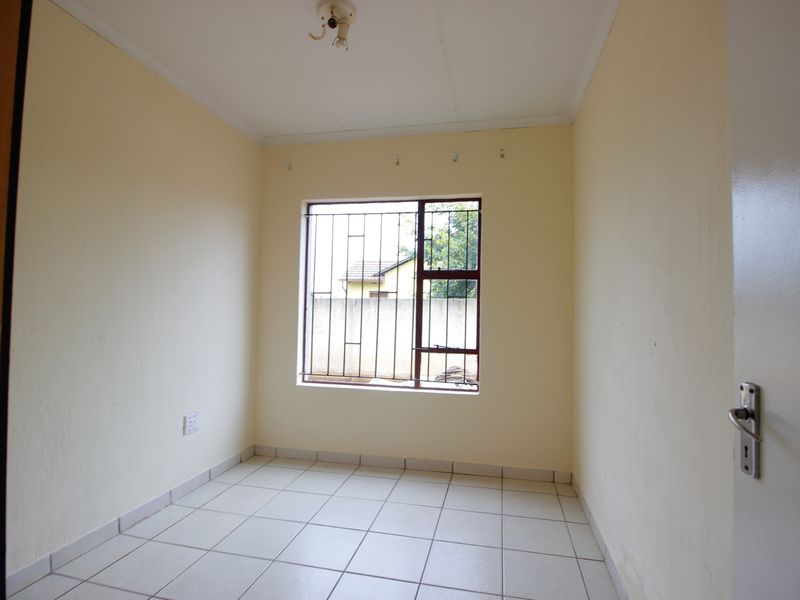 An empty bedroom featuring tiled flooring and security bars on the window, providing a blank canvas for potential interior design updates.