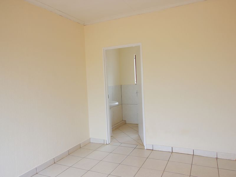 An empty bedroom featuring neutral wall paint and tiled flooring, with an open doorway leading to an adjacent bathroom area.
