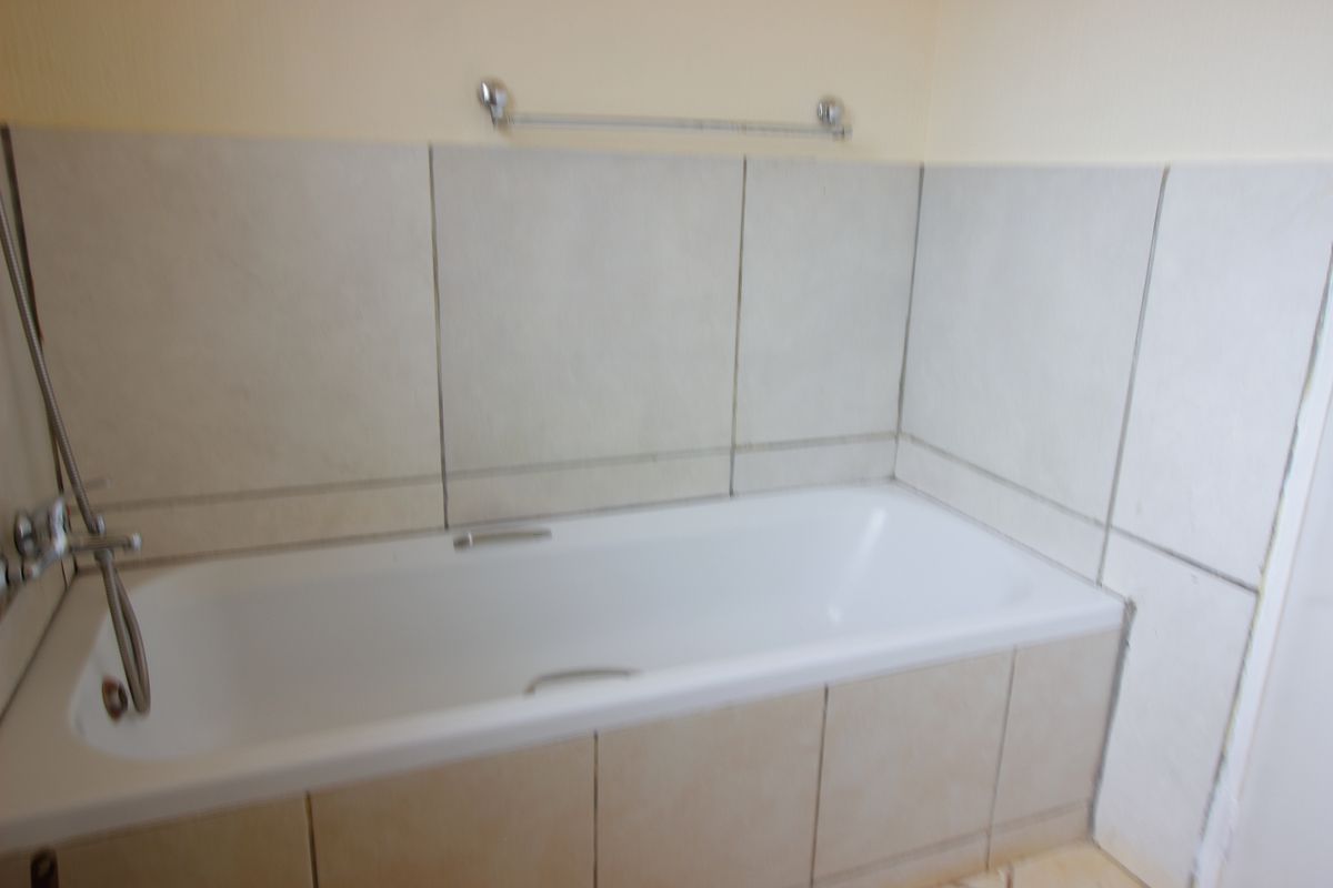 A functional bathroom featuring a built-in bathtub with tiled surround and apron, complemented by chrome fixtures and a wall-mounted towel rail.