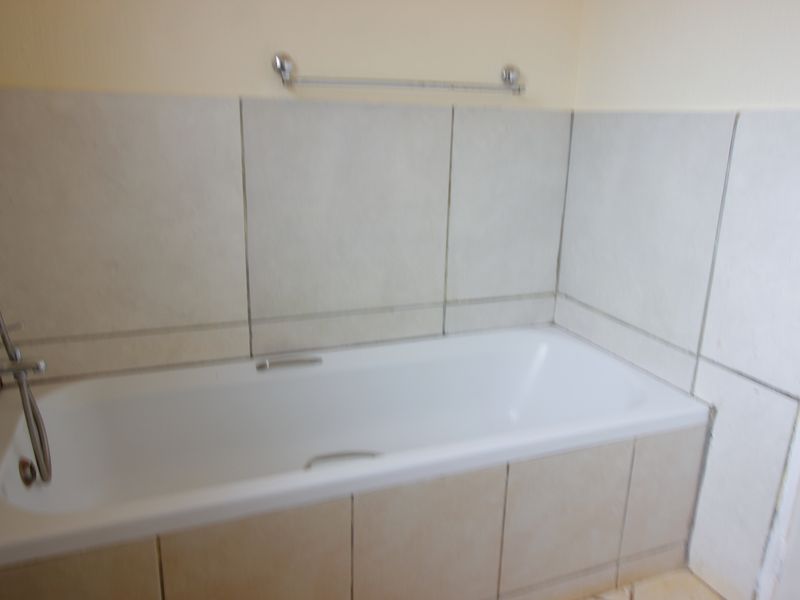 A functional bathroom featuring a built-in bathtub with tiled surround and apron, complemented by chrome fixtures and a wall-mounted towel rail.