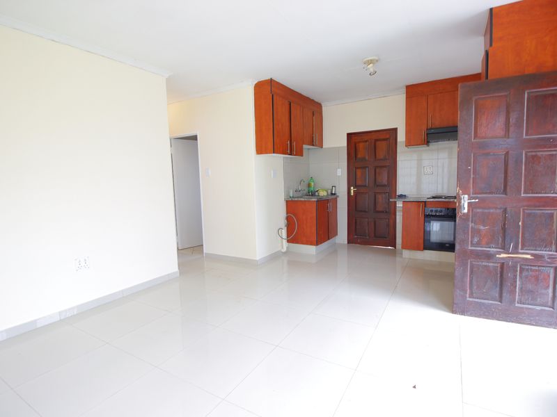 An open-plan living and kitchen area featuring tiled floors, built-in wooden cabinetry, and integrated cooking appliances.