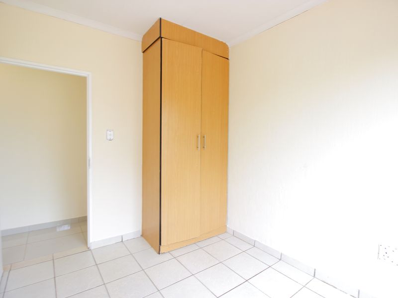 A clean, empty bedroom featuring neutral tiled flooring and a functional built-in wooden wardrobe.