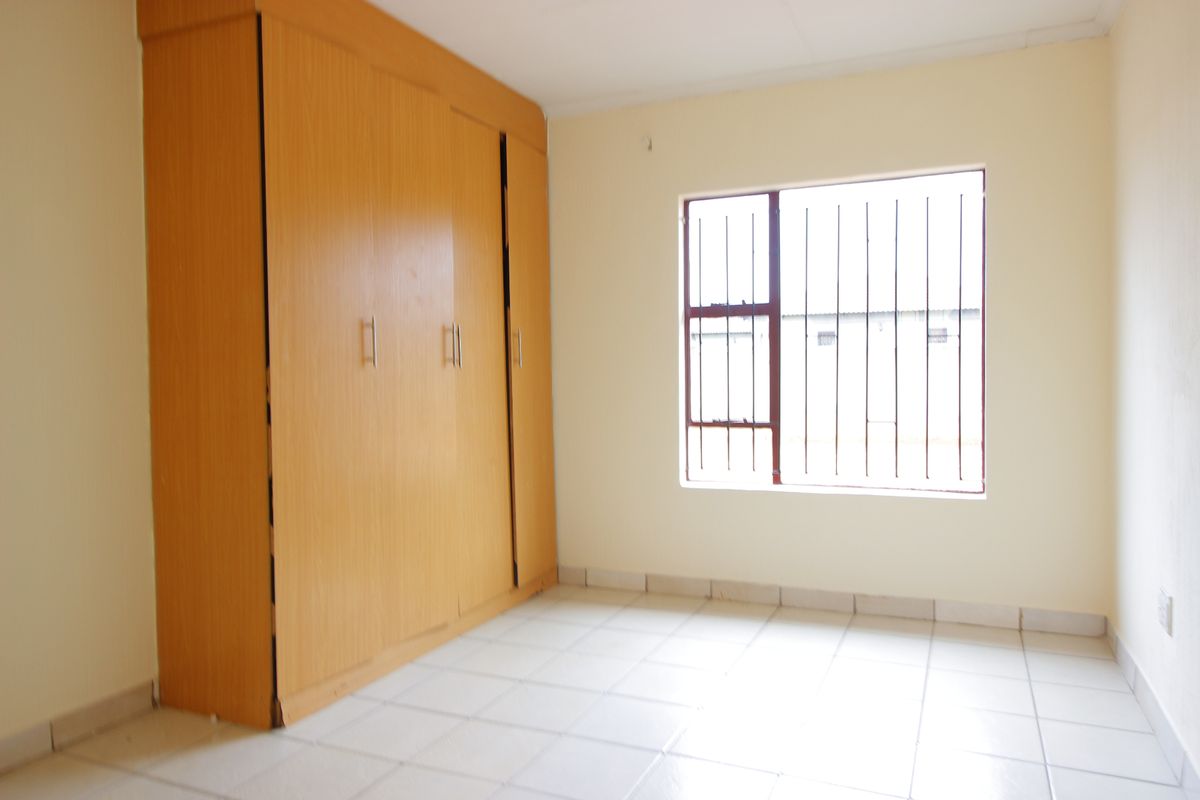 A vacant bedroom featuring tiled flooring, built-in wooden cupboards, and a window fitted with security bars.