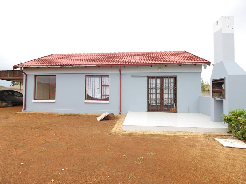 Rear exterior view featuring a tiled patio, built-in braai, and direct access to the home via security-gated doors.