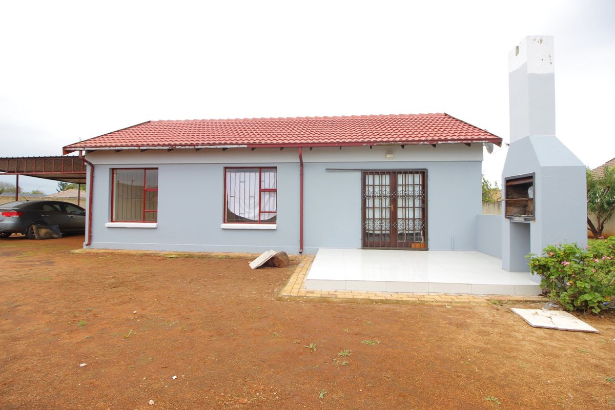 Rear exterior view featuring a tiled patio, built-in braai, and direct access to the home via security-gated doors.