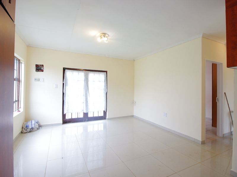 An empty, neutrally painted living room featuring tiled flooring, a ceiling light fixture, and double glass doors leading to the exterior.