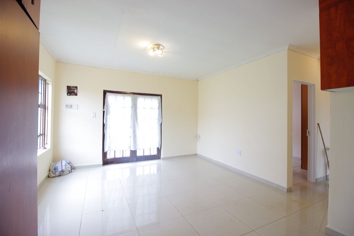 An empty, neutrally painted living room featuring tiled flooring, a ceiling light fixture, and double glass doors leading to the exterior.