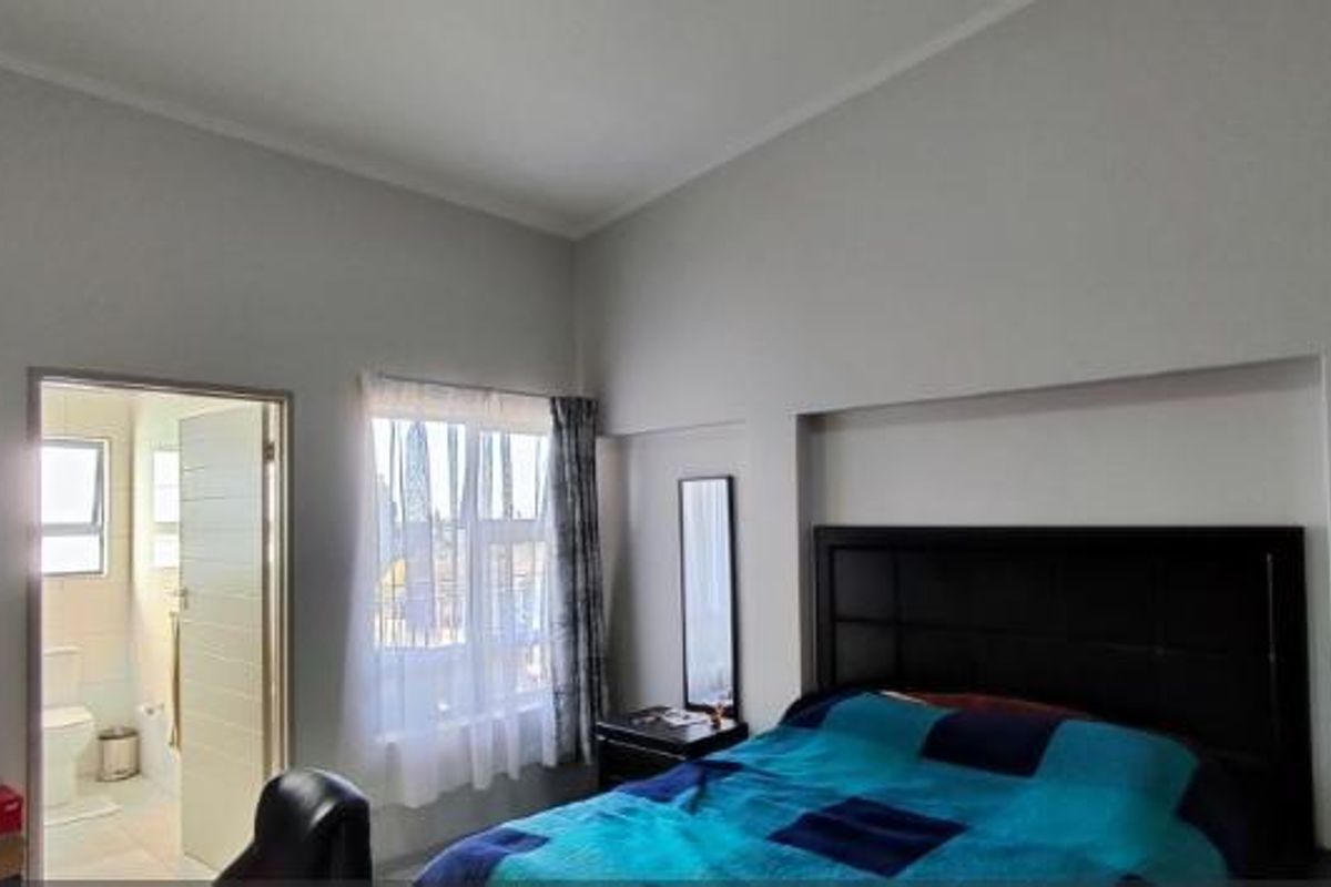 A spacious bedroom featuring high ceilings, a built-in headboard, and direct access to an en-suite bathroom.