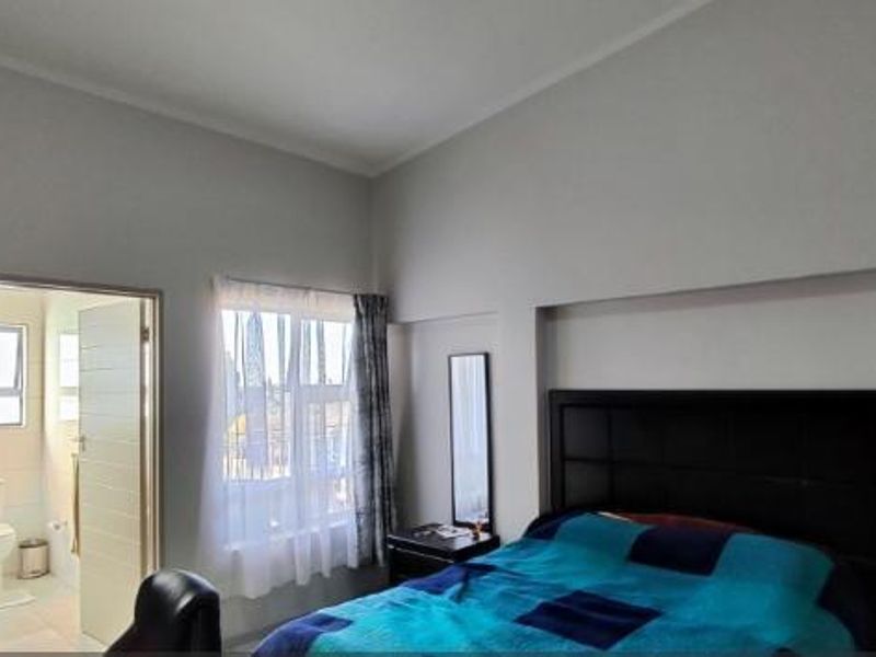 A spacious bedroom featuring high ceilings, a built-in headboard, and direct access to an en-suite bathroom.