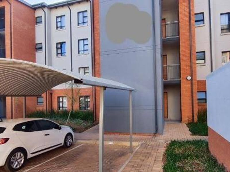 Exterior view of a modern apartment complex featuring a covered carport, paved parking area, and multi-story brick and rendered facade.