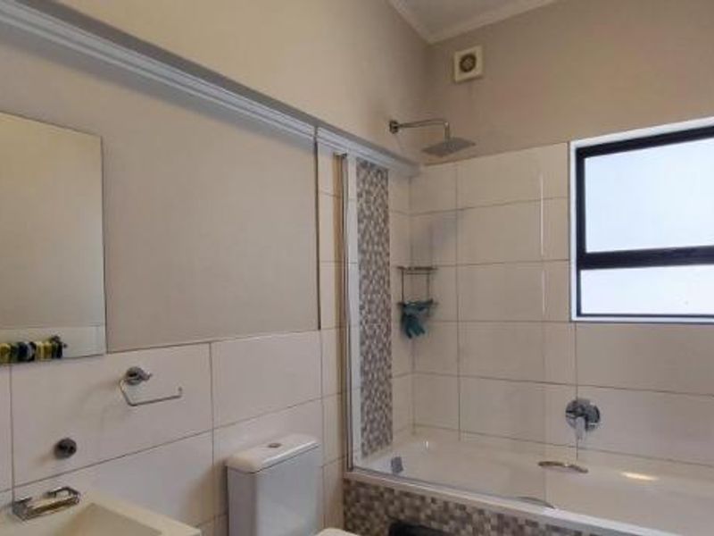 A functional bathroom featuring a built-in bathtub with shower head, wall-mounted toilet, vanity basin, and neutral tiled finishes.