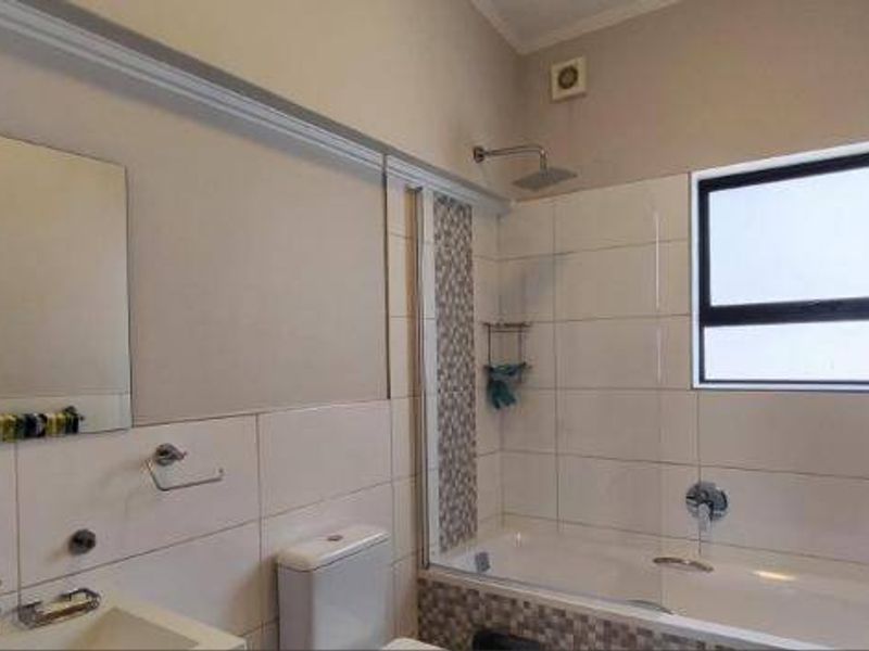 A clean, functional bathroom featuring a bathtub with shower head, wall-mounted vanity basin, and neutral wall tiling.
