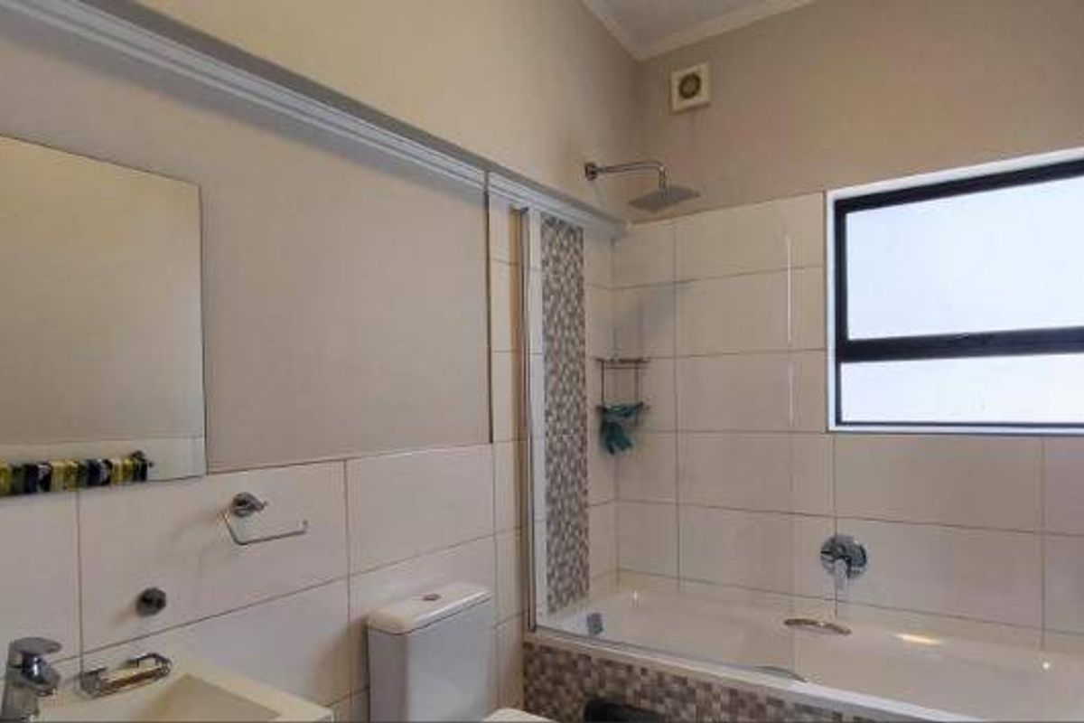 A clean, functional bathroom featuring a bathtub with shower head, wall-mounted vanity basin, and neutral wall tiling.