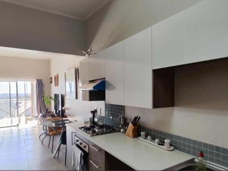 Open-plan kitchen and living area featuring modern white cabinetry, gas hob, tiled splashback, and sliding doors leading to an outdoor space.