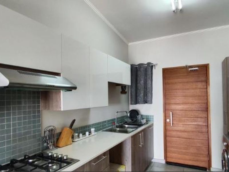 Modern kitchen featuring white cabinetry, a gas hob with extractor fan, tiled backsplash, and a solid wood door leading to the exterior.