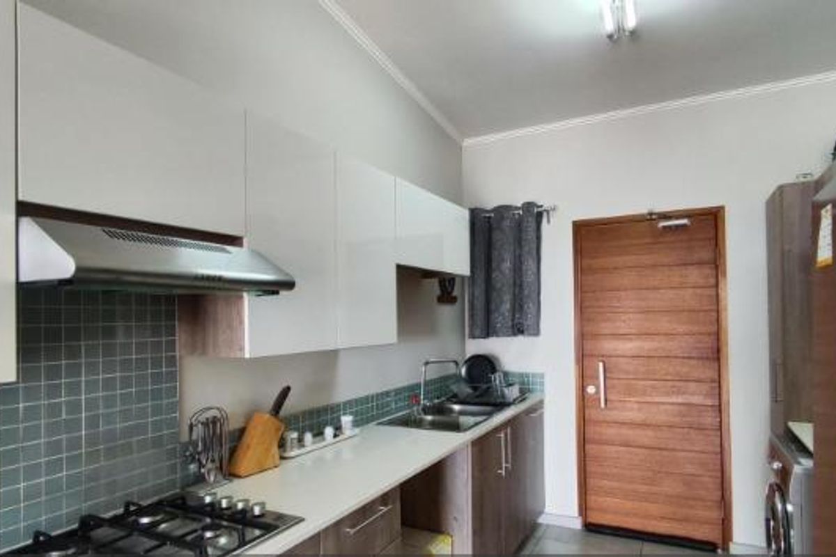 Modern kitchen featuring white cabinetry, a gas hob with extractor fan, tiled backsplash, and a solid wood door leading to the exterior.
