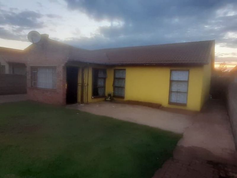 Front view of a single-story residential house featuring a tiled roof, yellow exterior walls, and a surrounding brick boundary wall.