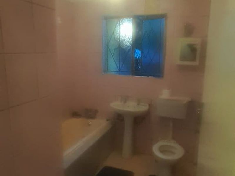 A dated bathroom featuring a pedestal basin, bathtub, and toilet with original wall and floor tiling.