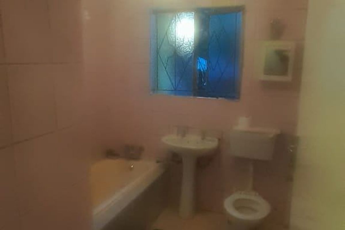 A dated bathroom featuring a pedestal basin, bathtub, and toilet with original wall and floor tiling.