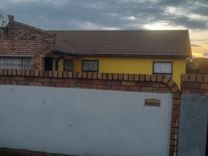 Front view of a single-story brick house featuring a tiled roof, security bars, and a gated perimeter wall.