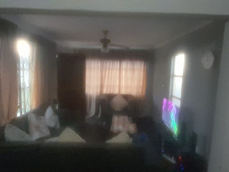 A dimly lit living room area featuring a ceiling fan and window security bars, requiring better lighting and professional photography to showcase the space.