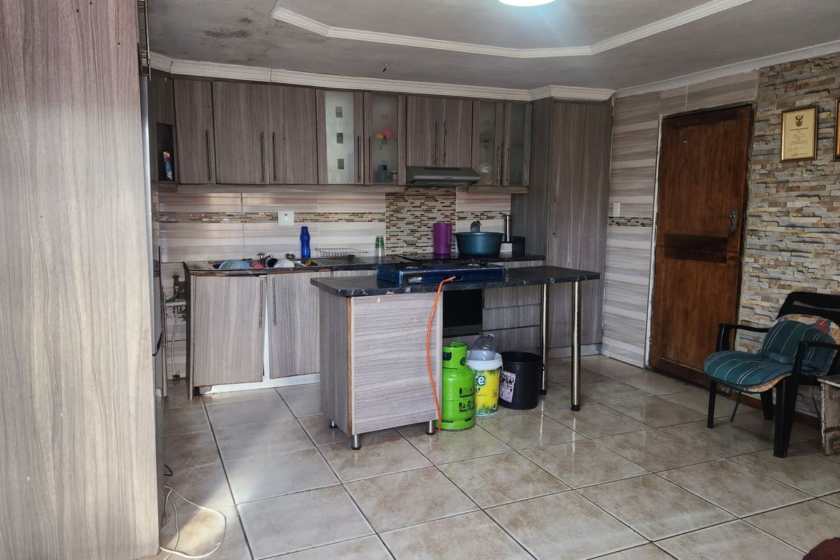 Kitchen featuring laminate cabinetry, stone-look tile flooring, and a stone veneer feature wall. The ceiling shows visible signs of water damage.