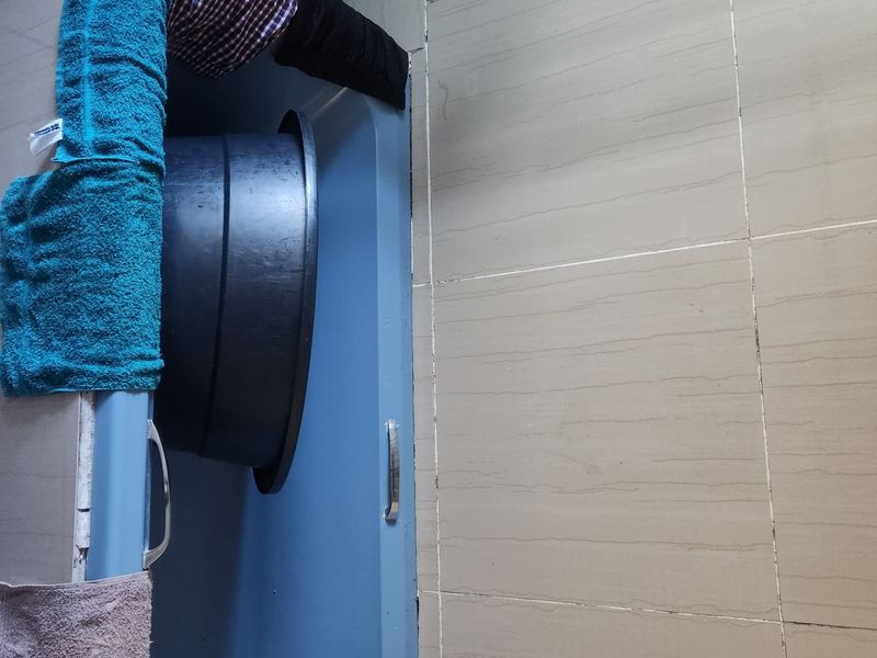 A bathroom featuring a blue bathtub and neutral ceramic wall tiling, requiring updates to finishes and fixtures.