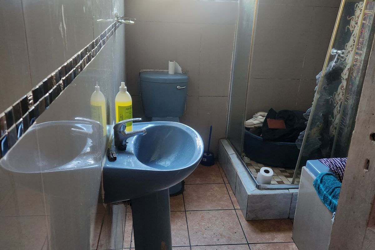 A functional bathroom featuring a pedestal basin, toilet, and shower enclosure with tiled walls and flooring, currently showing signs of wear and dated finishes.