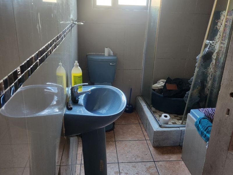 A functional bathroom featuring a pedestal basin, toilet, and shower enclosure with tiled walls and flooring, currently showing signs of wear and dated finishes.