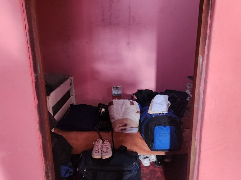 A small bedroom space featuring pink painted walls and a single electrical outlet, currently used for storage.