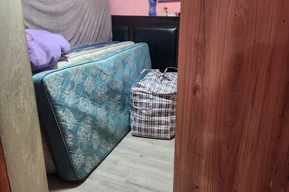 A small bedroom featuring laminate flooring and pink wall finishes, currently used for storage.
