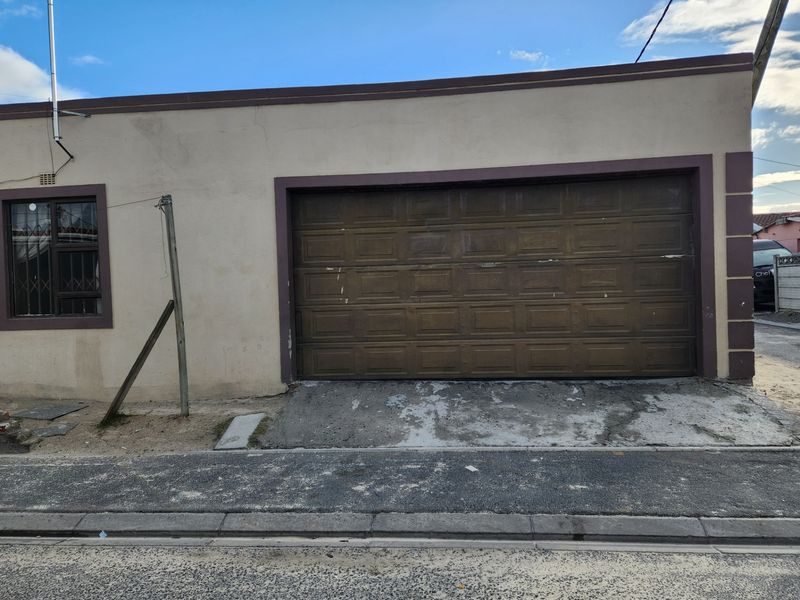 Street-facing view of a single garage with a sectional door, security-barred window, and a weathered concrete driveway.