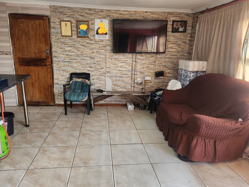 A living room featuring a stone-cladding accent wall, ceramic floor tiles, and a wooden door, providing a functional space with potential for aesthetic updates.