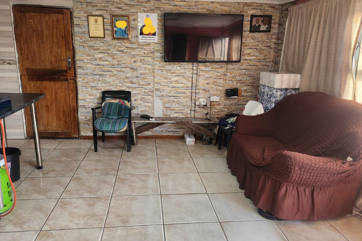 A living room featuring a stone-cladding accent wall, ceramic floor tiles, and a wooden door, providing a functional space with potential for aesthetic updates.