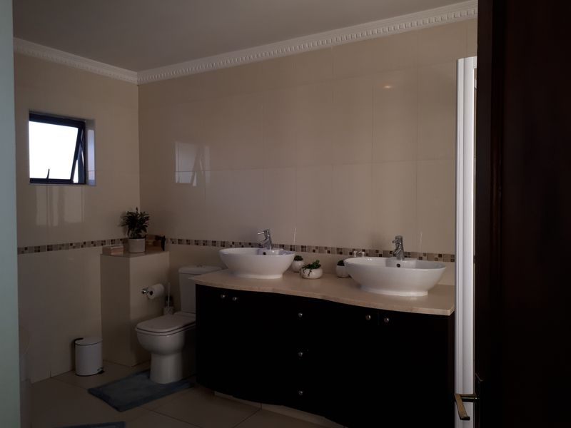 A well-maintained bathroom featuring a double vanity with vessel sinks, chrome fixtures, tiled walls, and a casement window for natural light.