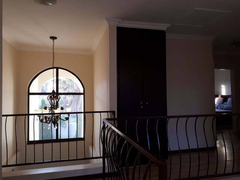 A spacious landing area featuring an arched window, wrought iron balustrade, and built-in storage cabinetry with crown molding details.