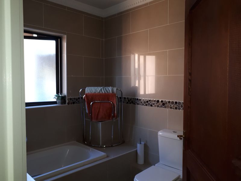 A functional bathroom featuring a built-in bathtub, a toilet, and neutral ceramic wall tiles with a decorative mosaic border.