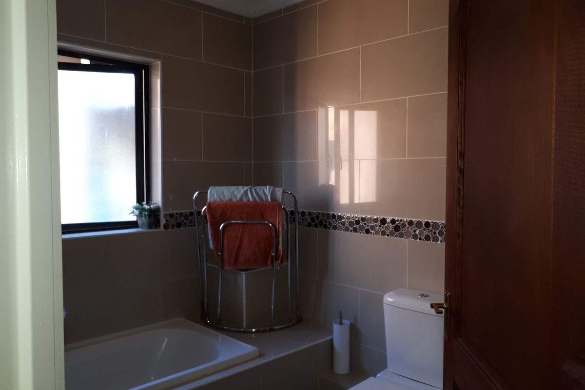 A functional bathroom featuring a built-in bathtub, a toilet, and neutral ceramic wall tiles with a decorative mosaic border.