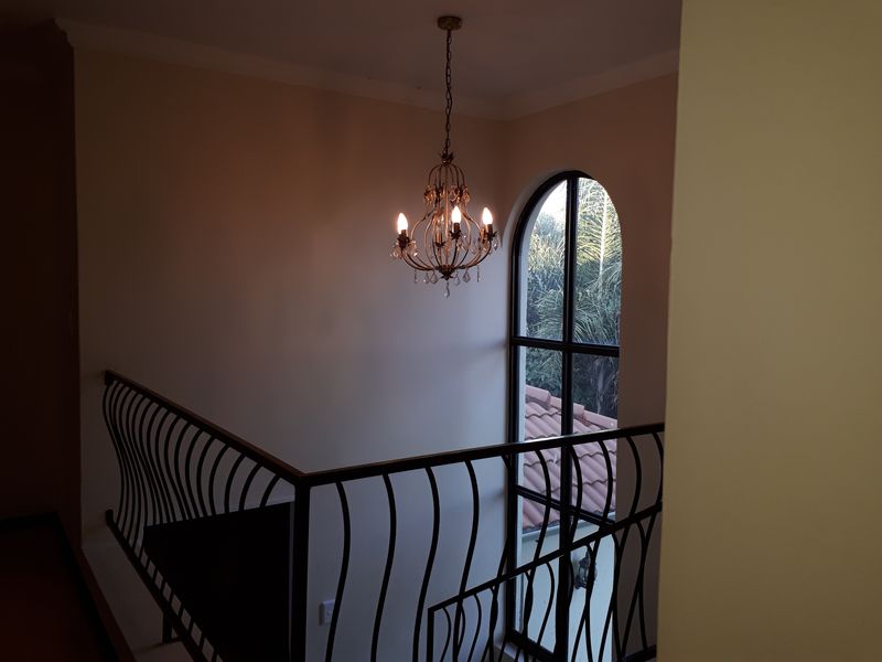 A landing area featuring a decorative wrought iron balustrade, an elegant chandelier, and a tall arched window overlooking the exterior.