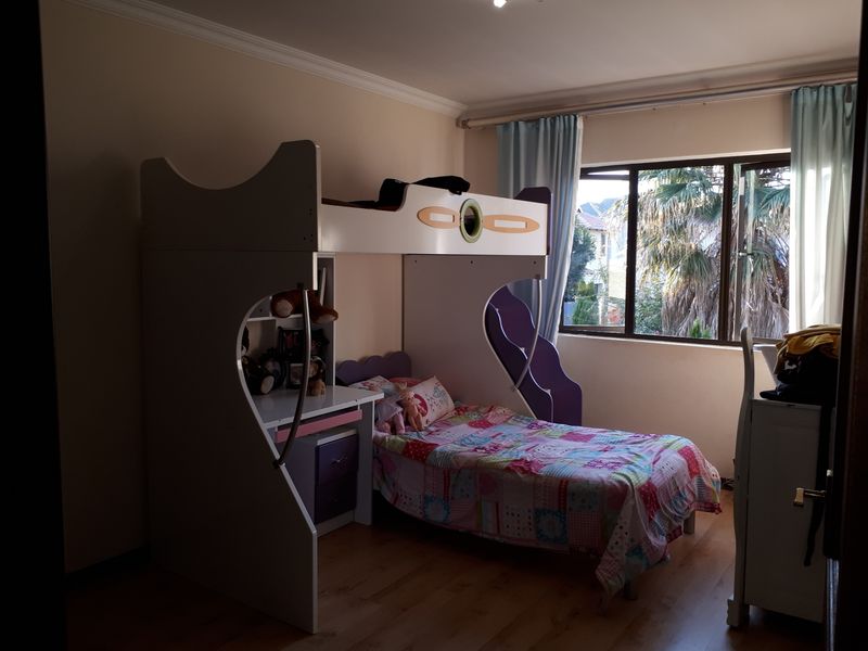 A bedroom featuring laminate flooring, cornice detailing, and an aluminium-framed window providing natural light.