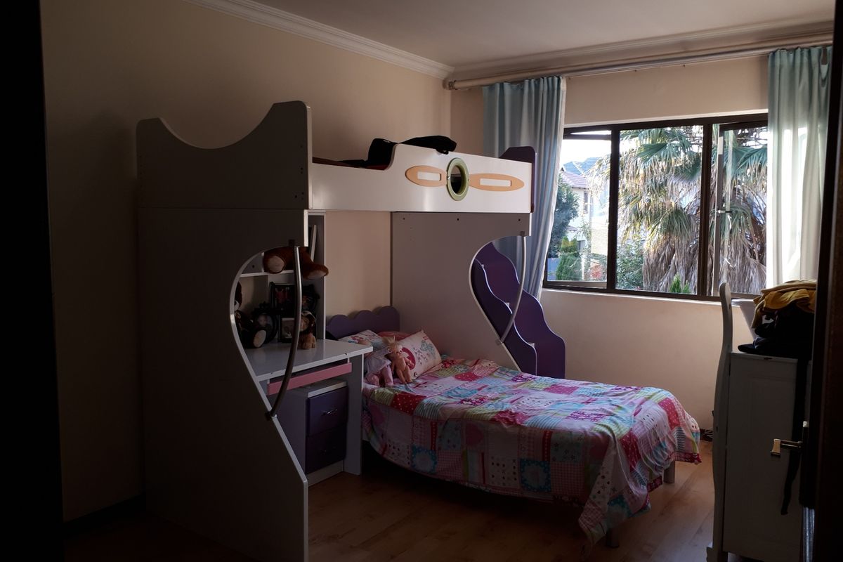 A bedroom featuring laminate flooring, cornice detailing, and an aluminium-framed window providing natural light.