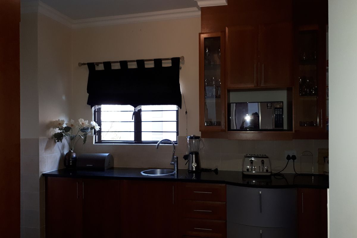 A functional kitchen featuring dark wood cabinetry, granite countertops, a built-in microwave, and a tiled backsplash with a window overlooking the exterior.