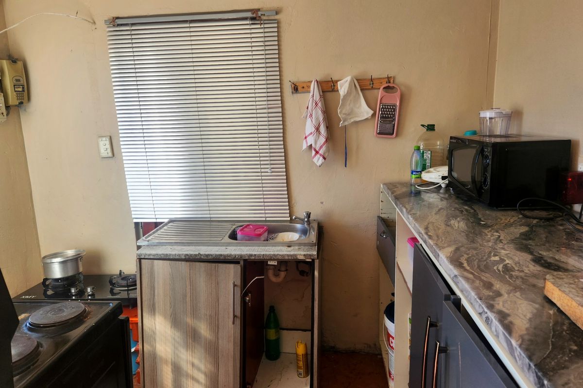 A compact kitchen area featuring a stainless steel sink, laminate countertops, and tiled flooring, currently requiring maintenance and cosmetic updates to the cabinetry.