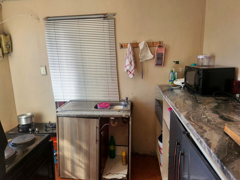 A compact kitchen area featuring a stainless steel sink, laminate countertops, and tiled flooring, currently requiring maintenance and cosmetic updates to the cabinetry.