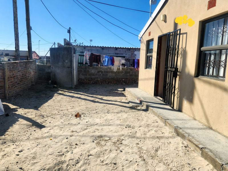Rear exterior view of the property featuring a sandy yard, concrete apron, and security gate access.