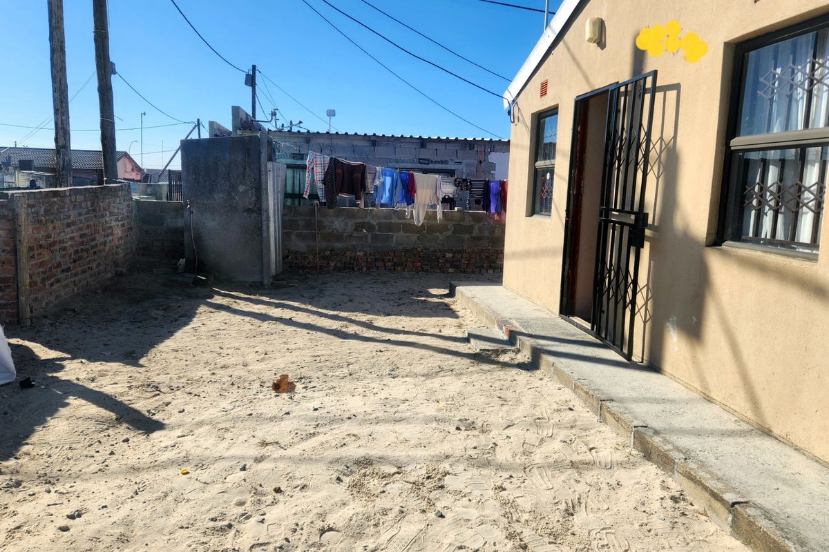 Rear exterior view of the property featuring a sandy yard, concrete apron, and security gate access.