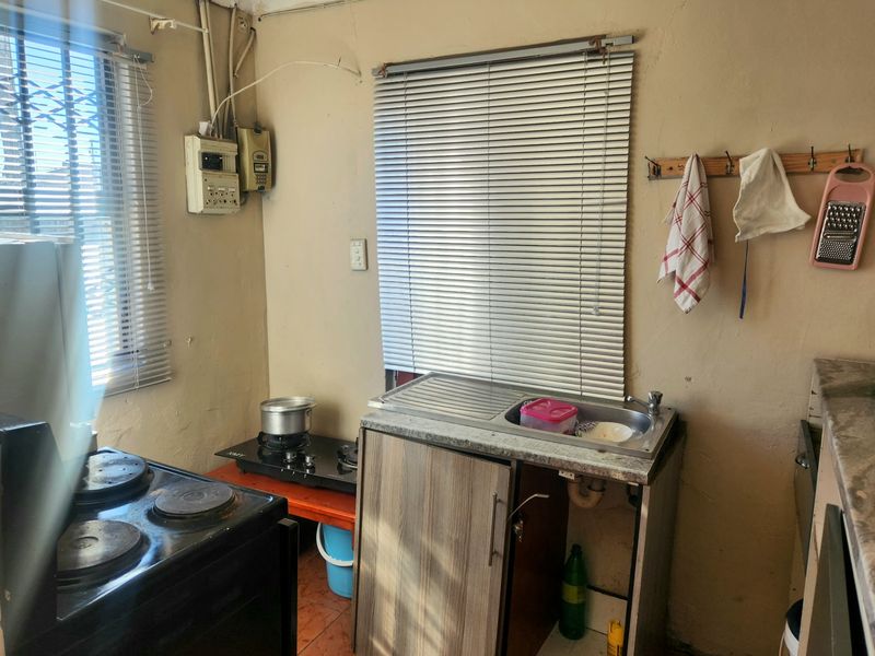 A compact kitchen area featuring a stainless steel sink, electric stove, and tiled flooring, requiring significant maintenance and cosmetic updates.