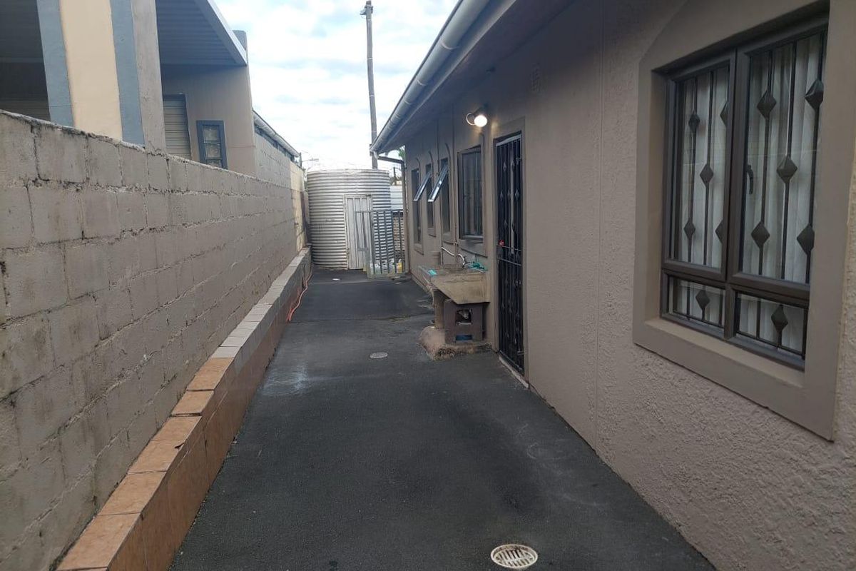 A narrow paved side passage featuring a utility sink, security gates, and a water tank, enclosed by a concrete boundary wall.