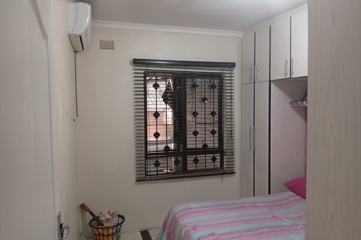 A functional bedroom featuring built-in cupboards, an air conditioning unit, and security burglar bars on the window.