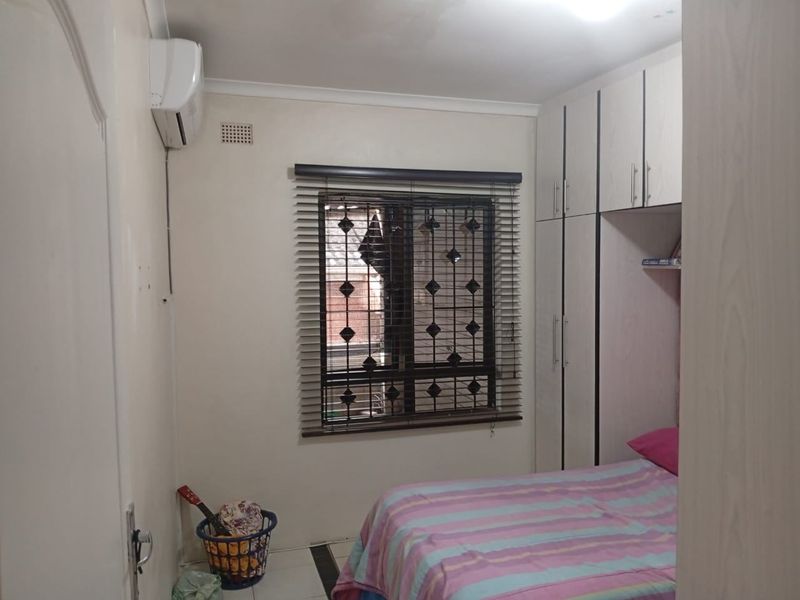 A functional bedroom featuring built-in cupboards, an air conditioning unit, and security burglar bars on the window.